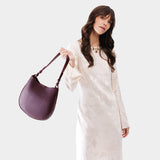 Plum Medium | Woman wearing rounded shoulder bag with adjustable strap on a white background