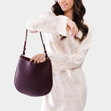 Plum Medium | Woman wearing rounded shoulder bag with adjustable strap on a white background