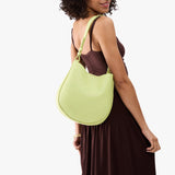 Shadow Lime Medium | Model carrying round leather purse with adjustable shoulder strap