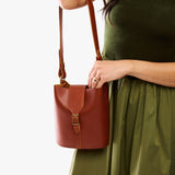 Chestnut | Model wearing leather bucket shoulder bag with adjustable strap and magnetic closure 