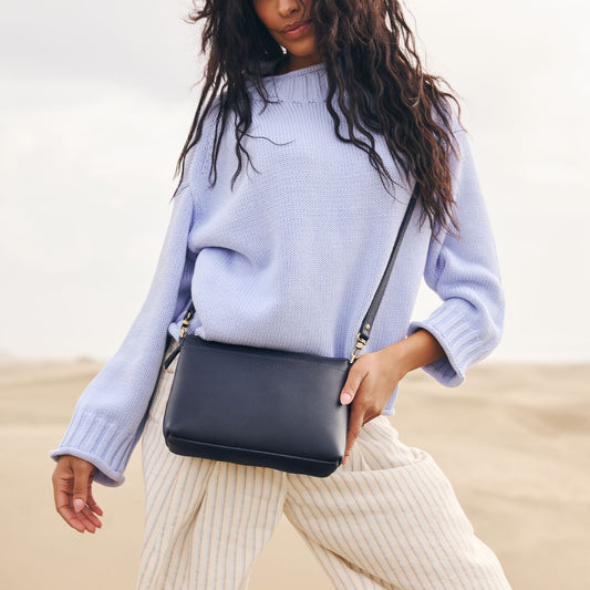 A model standing on the beach wearing a Night Owl Poppy Purse.