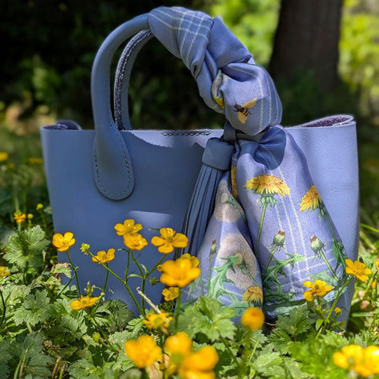 Blue handbag with a floral ribbon in a field of yellow flowers