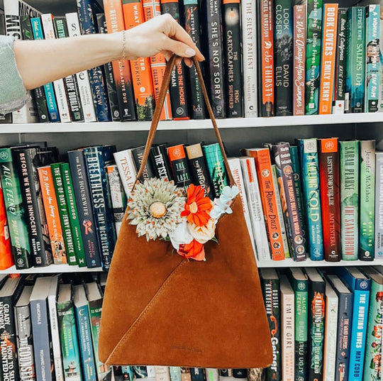 Brown handbag with floral decorations held in front of a bookshelf filled with books.