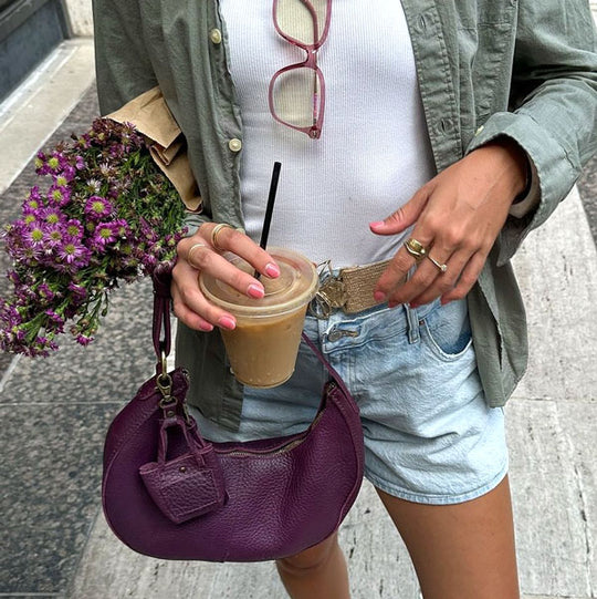 Person holding a purple handbag, coffee cup, and flowers on a sidewalk.