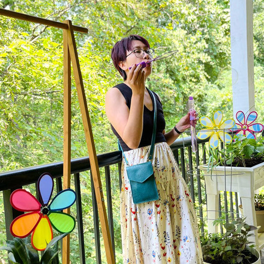 Woman on a balcony with colorful wind spinners and plants wearing a crossbody bag