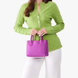 Cattleya Small | Model holding a petite tote purse with structured leather handles and crossbody strap