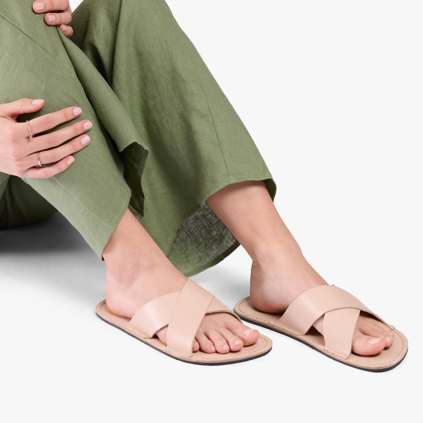 Crema | Close-up of model wearing light green pants and beige flat sandals, shown against a plain background