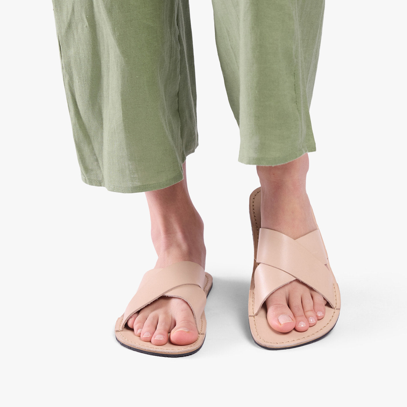 Crema | Close-up of model wearing light green pants and beige flat sandals, shown against a plain background
