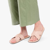 Crema | Close-up of model wearing light green pants and beige flat sandals, shown against a plain background