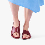 Marsala | Close-up of model wearing light blue dress and reddish brown flat sandals, shown against a plain background