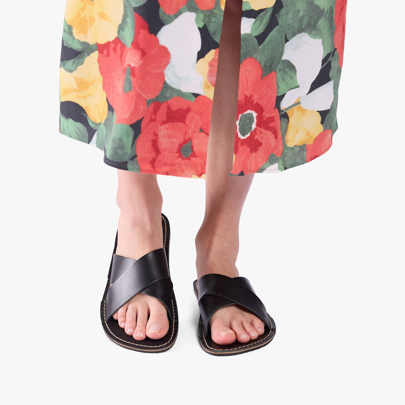 Nero | Close-up of model wearing floral print dress and black flat sandals, shown against a plain background