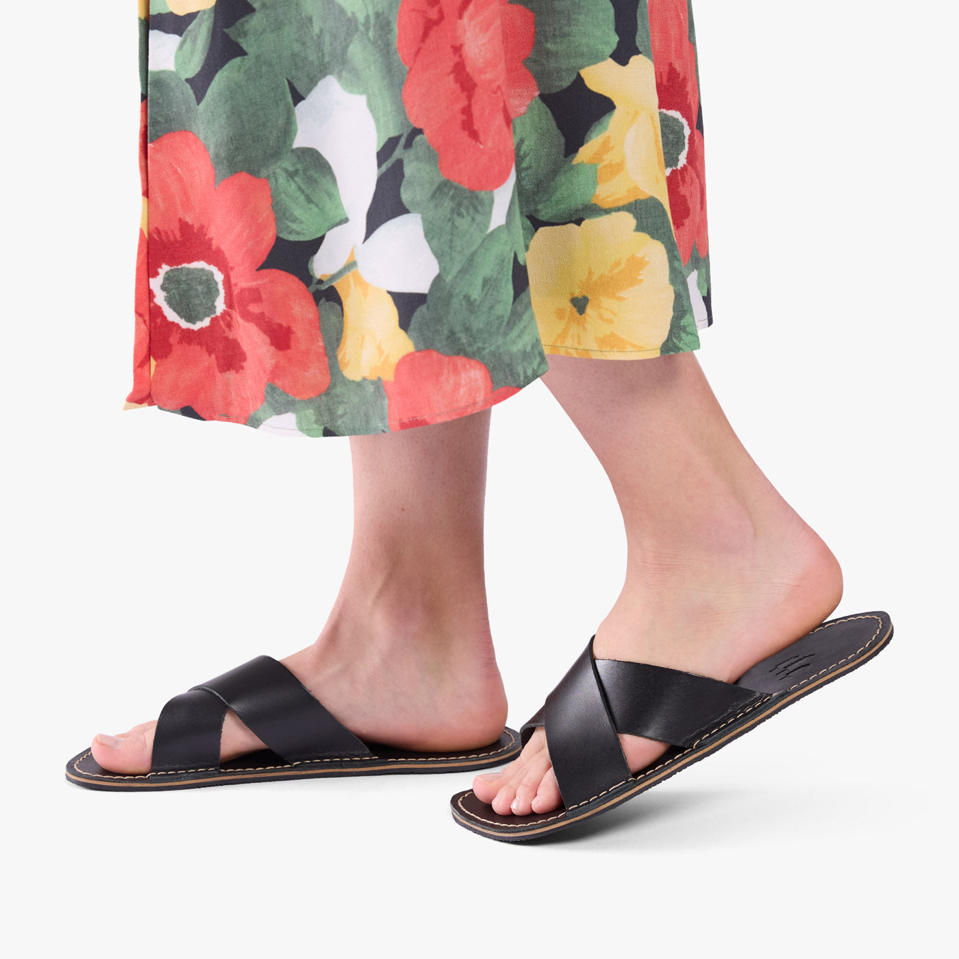 Nero | Close-up of model wearing floral print dress and black flat sandals, shown against a plain background