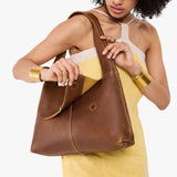 Asheville Medium | A model holding a slouchy triangle shaped shoulder bag with a flap