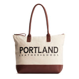 Canvas tote with zipper, leather bottom, and leather handles on a white background