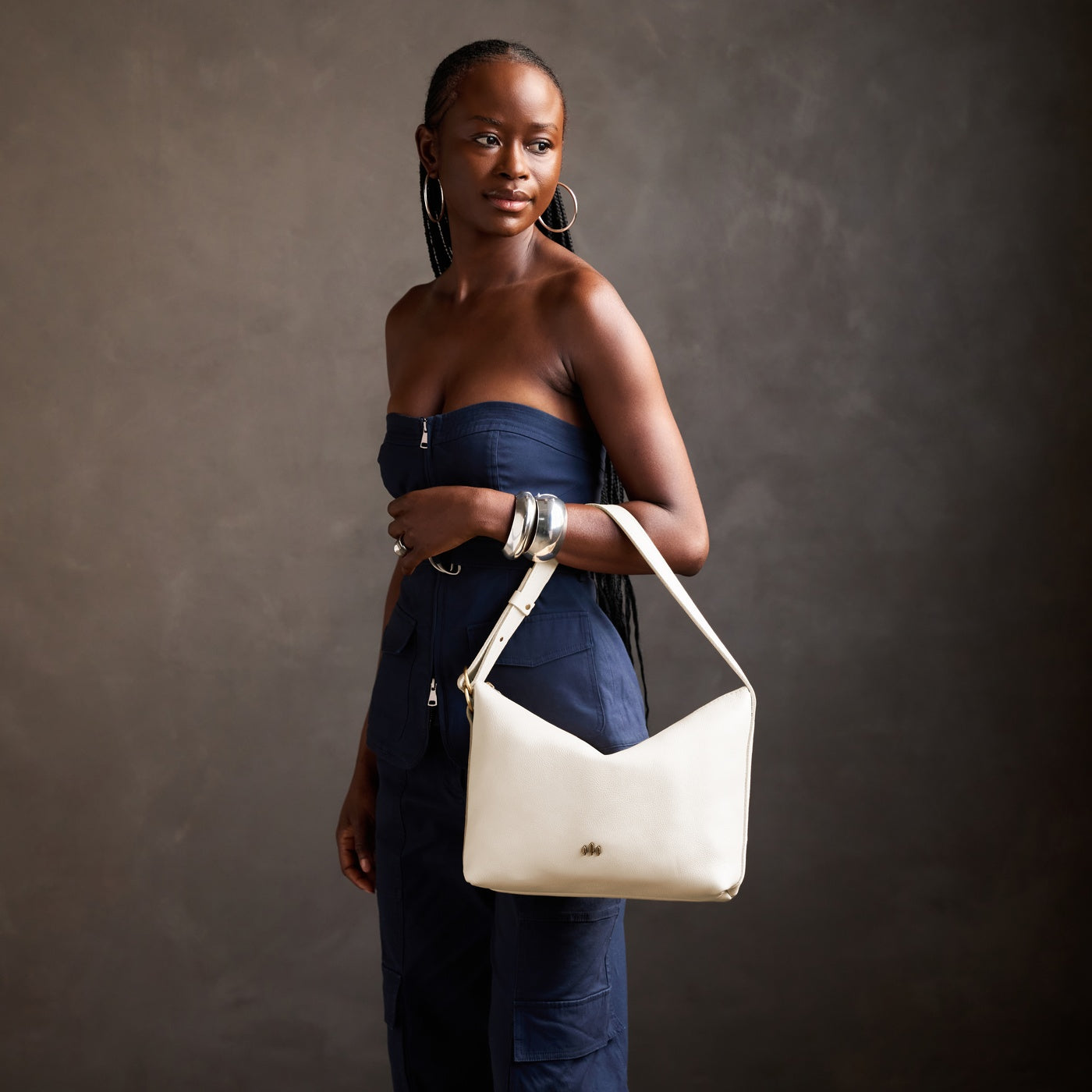 Pebbled Bone*Large | Model Wearing medium sized slouchy leather shoulder bag with zipper opening and three metal tree emblems