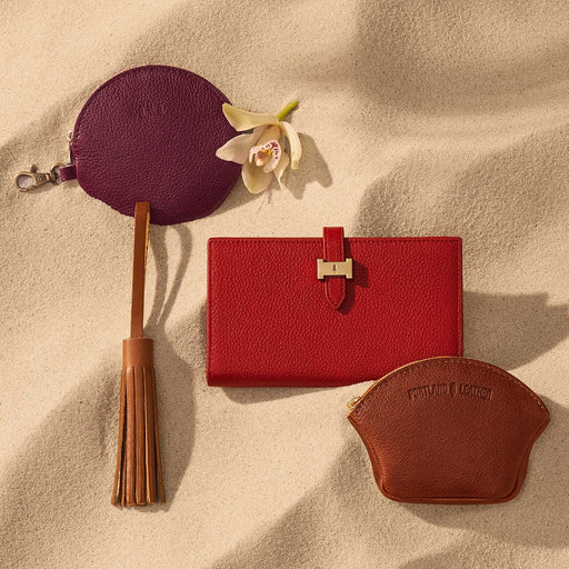 Group of leather small goods containing pouches, a wallet and tassel on sand featured image