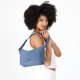 Denim Small | Model holding a Slouchy Shoulder Bag that has a zipper opening and three metal tree emblems
