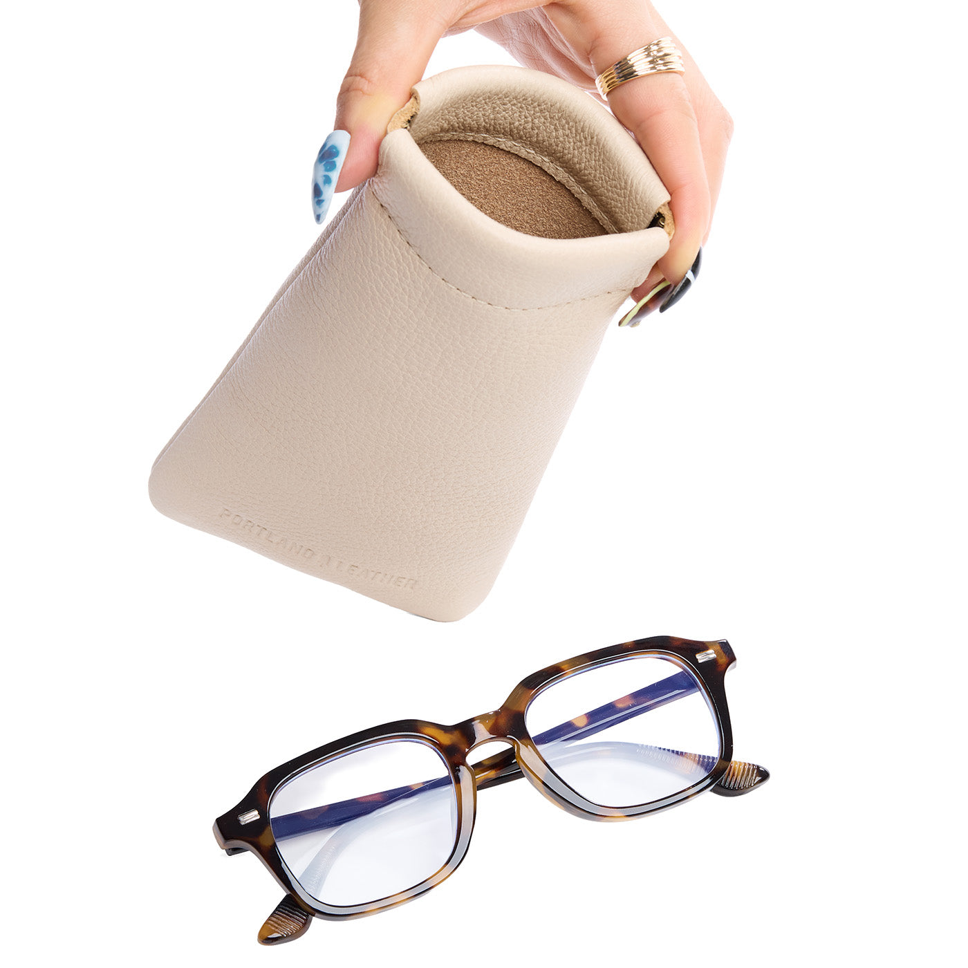 Pebbled Bone | Model hand holding open leather glasses case with hidden metal spring closure above a pair of glasses
