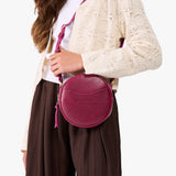 Orchid | Model wearing a circle shaped crossbody bag with top zipper and gold accents