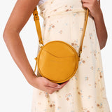Sunshine | Model wearing a circle shaped crossbody bag with top zipper and gold accents