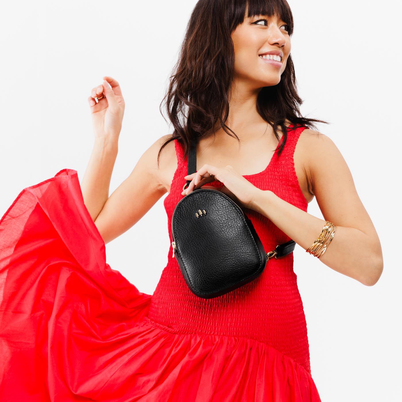 Pebbled--black  | Model wearing small sling bag with zipper closure and adjustable strap on the front of her body
