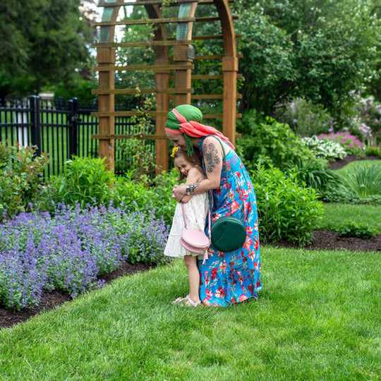 Adult and child in a garden with a wooden arch and greenery, both wearing Circle Crossbody Bags.
