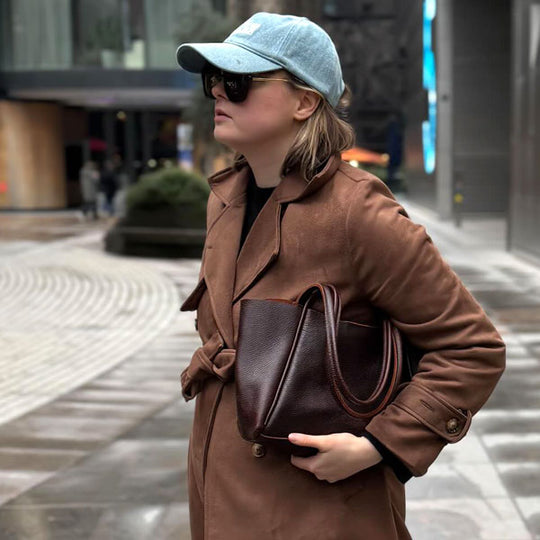Woman wearing sunglasses and a light blue baseball cap, holding a dark brown leather handbag.