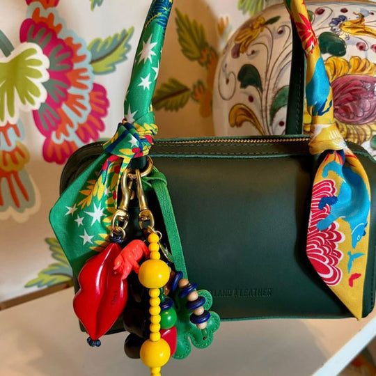 A green leather handbag decorated with colorful beads, printed fabric, and a red lips-shaped keychain.