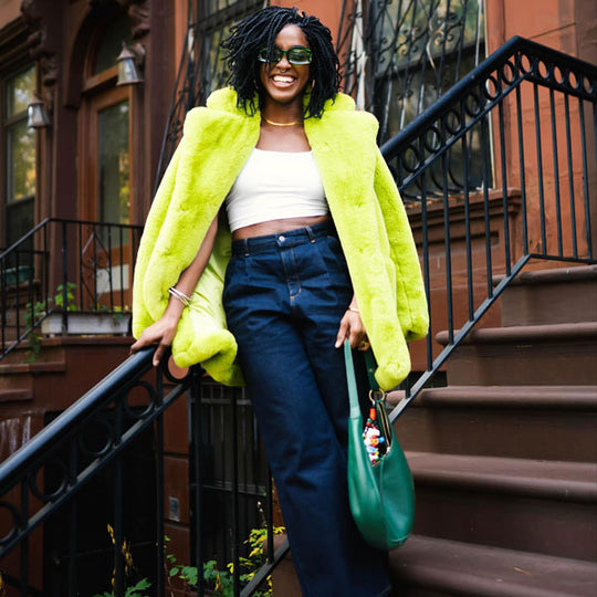 Person in a bright green jacket standing on the stairs and holding a green purse