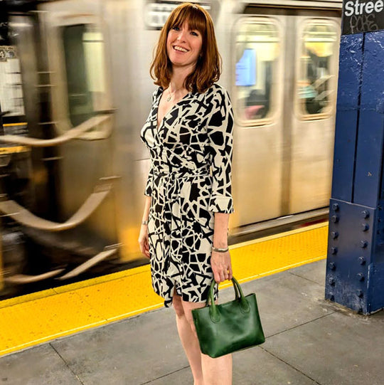 Woman standing at the train station, wearing a black and white dress holding a green leather handbag.