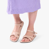 Crema | Close-up of model wearing light purple dress and beige flat sandals with an ankle strap and buckle, shown against a plain background
