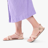 Crema | Close-up of model wearing light purple dress and beige flat sandals with an ankle strap and buckle, shown against a plain background