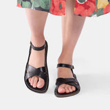 Nero | Close-up of model wearing floral-print dress and black flat sandals with an ankle strap and buckle, shown against a plain background
