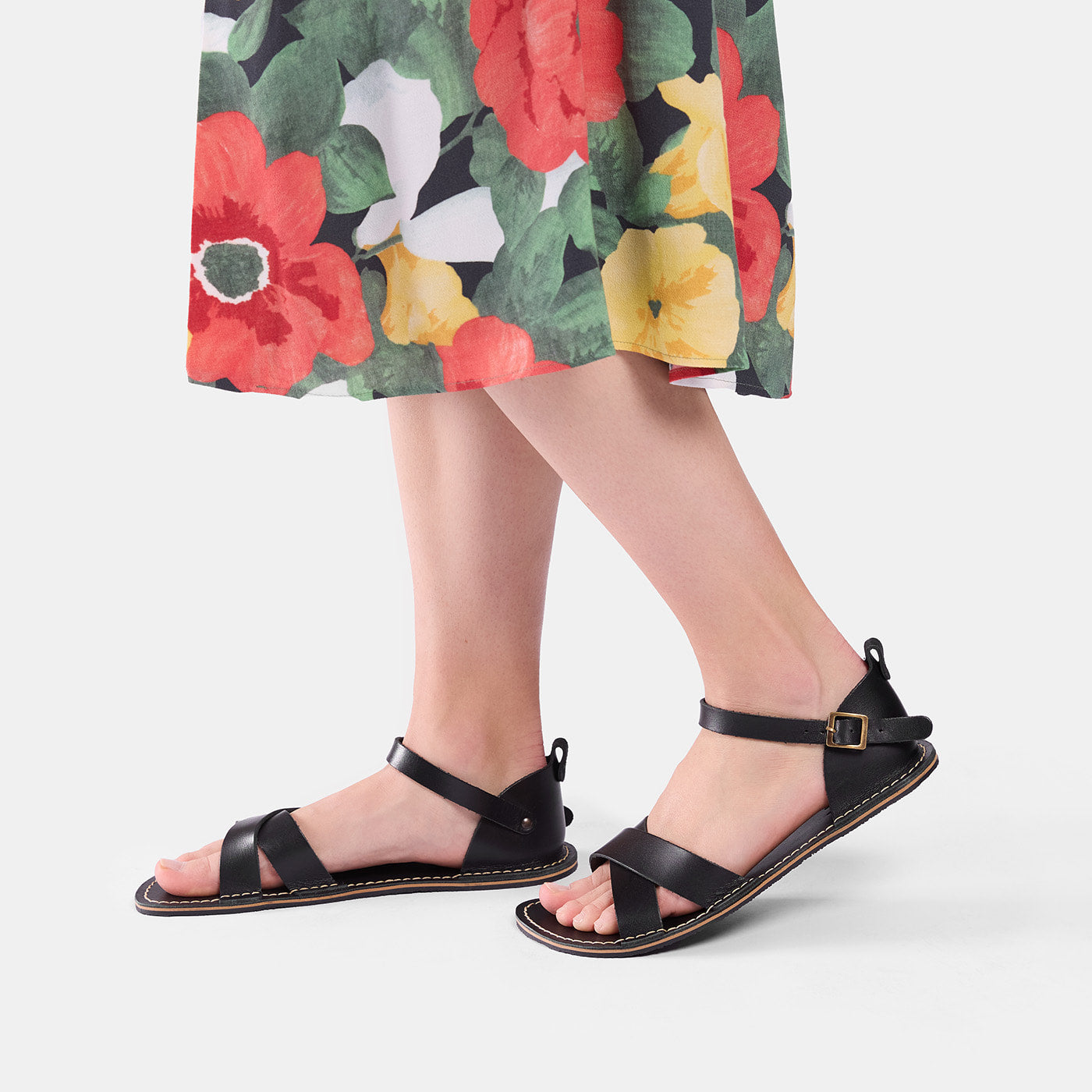 Nero | Close-up of model wearing floral-print dress and black flat sandals with an ankle strap and buckle, shown against a plain background