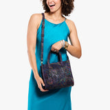 Carnival | Model holding structured mid-size tote bag with overlapping panels and crossbody strap
