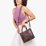 Sepia | Model holding structured mid-size tote bag with overlapping panels and crossbody strap